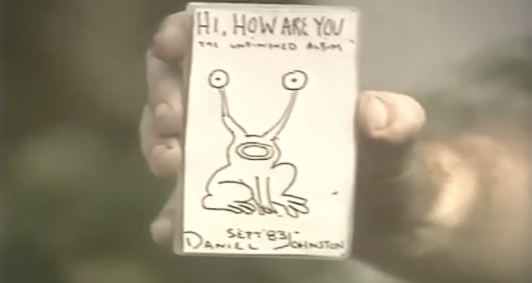 Daniel Johnston holds up the cover of Hi, How Are You